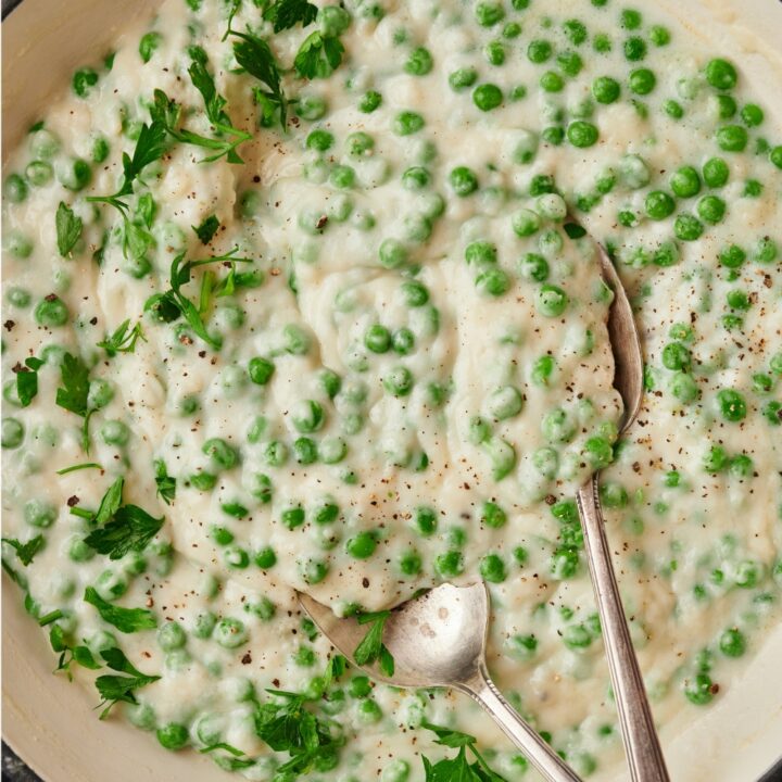 A close up of creamed peas in a skillet with a set of serving spoons in it.