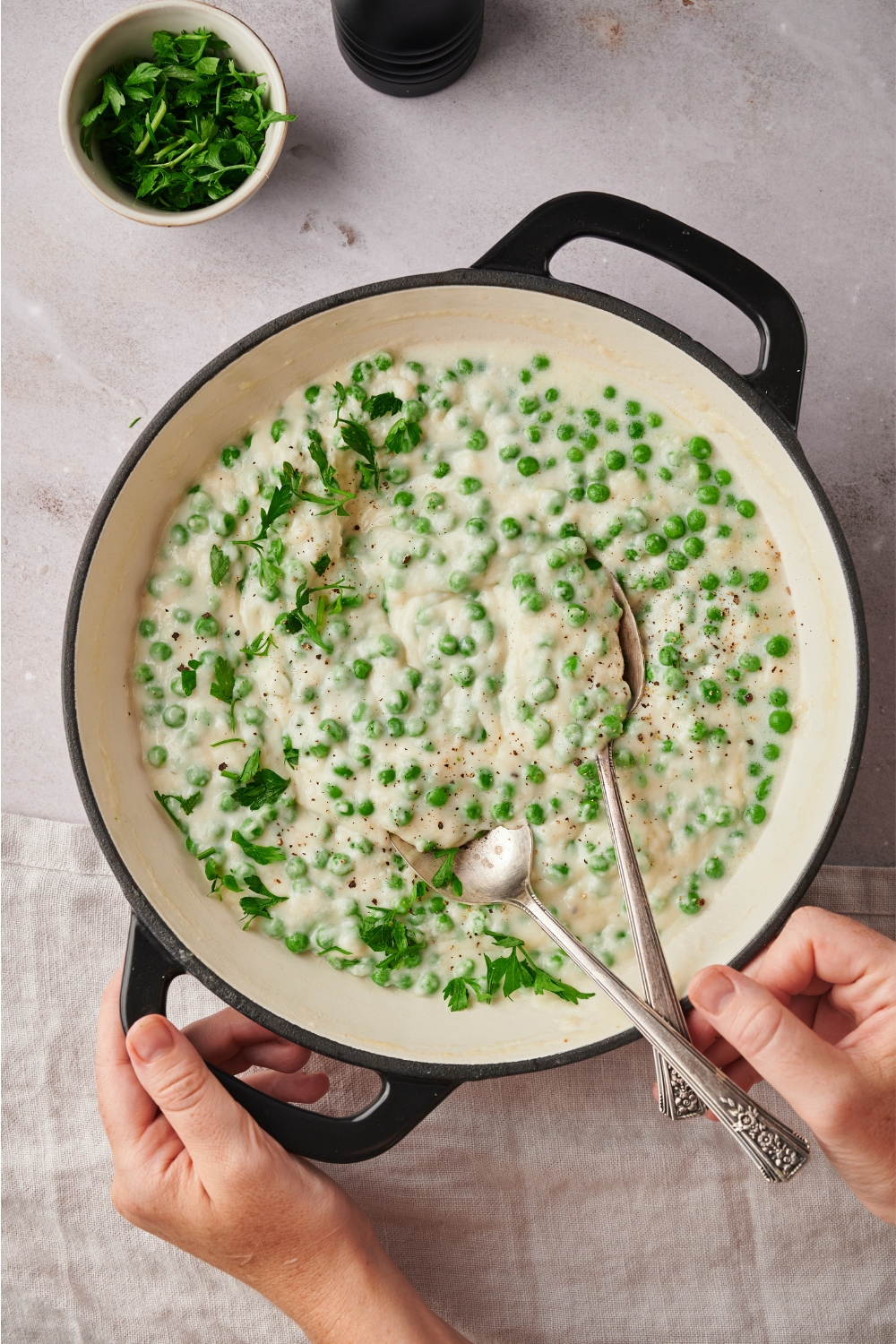 Creamed peas in a skillet with a set of serving spoons in it.