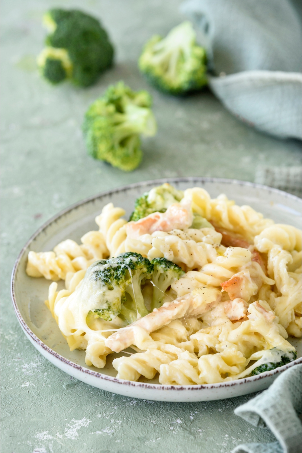 A plate of pasta in cream sauce with chicken strips and broccoli florets covered in cheese.