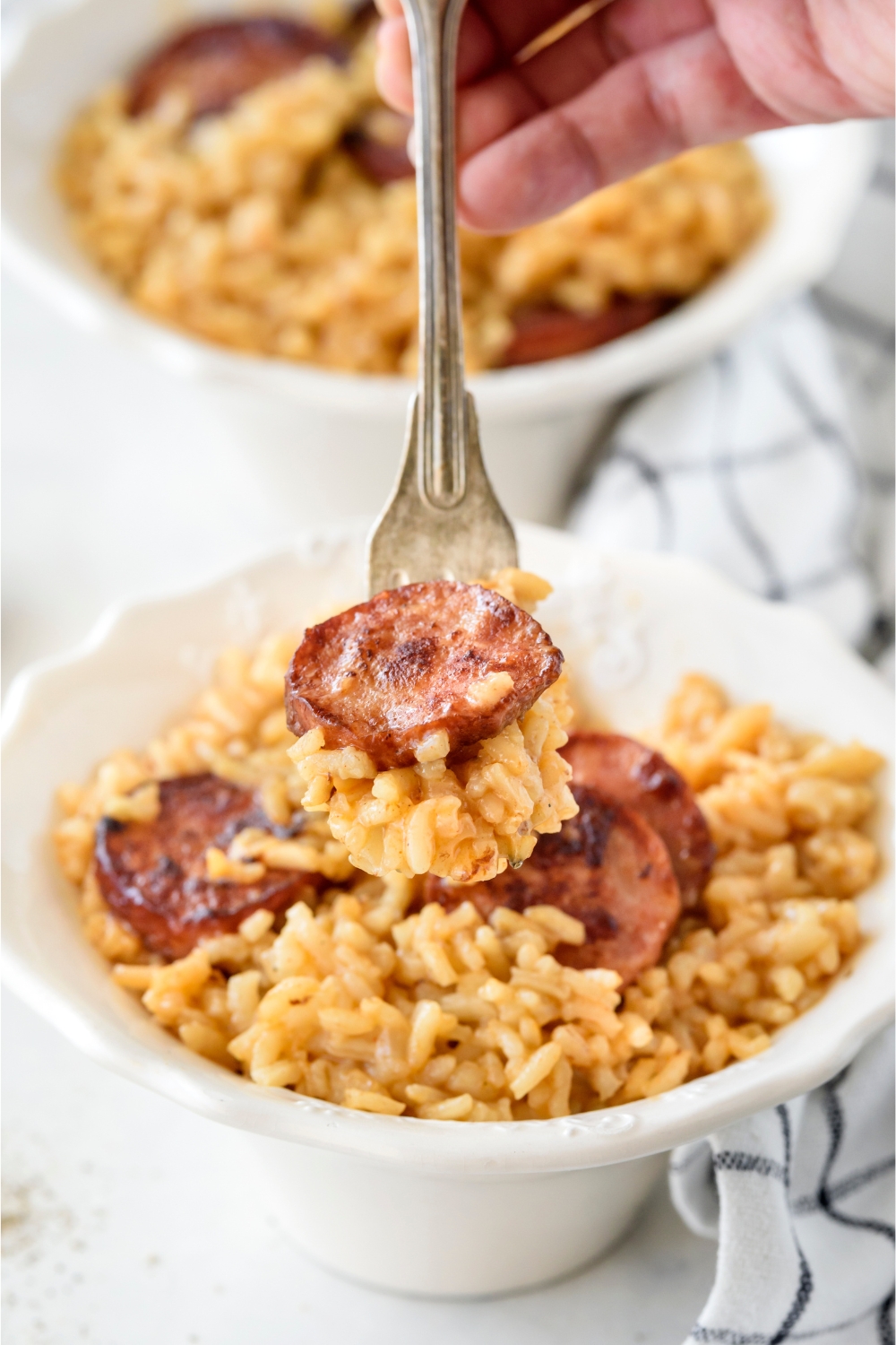 A fork holding a scoop of dirty rice with a cooked sausage slice on top.