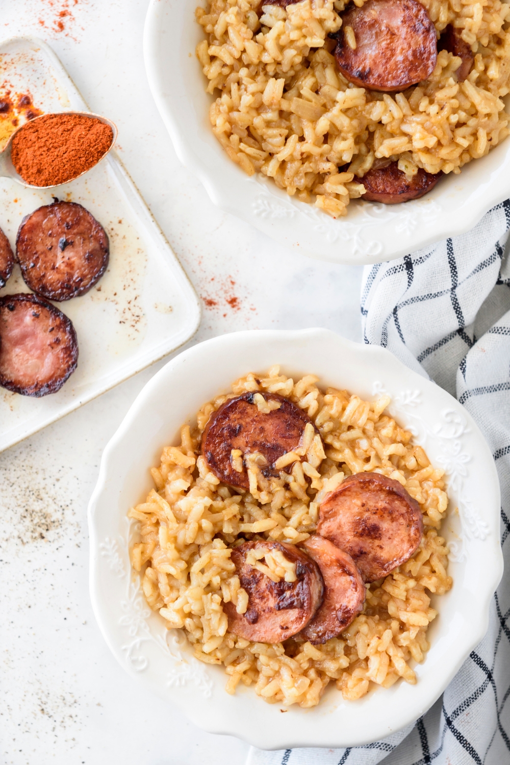 Two bowls of dirty rice with cooked sausage slices on top.