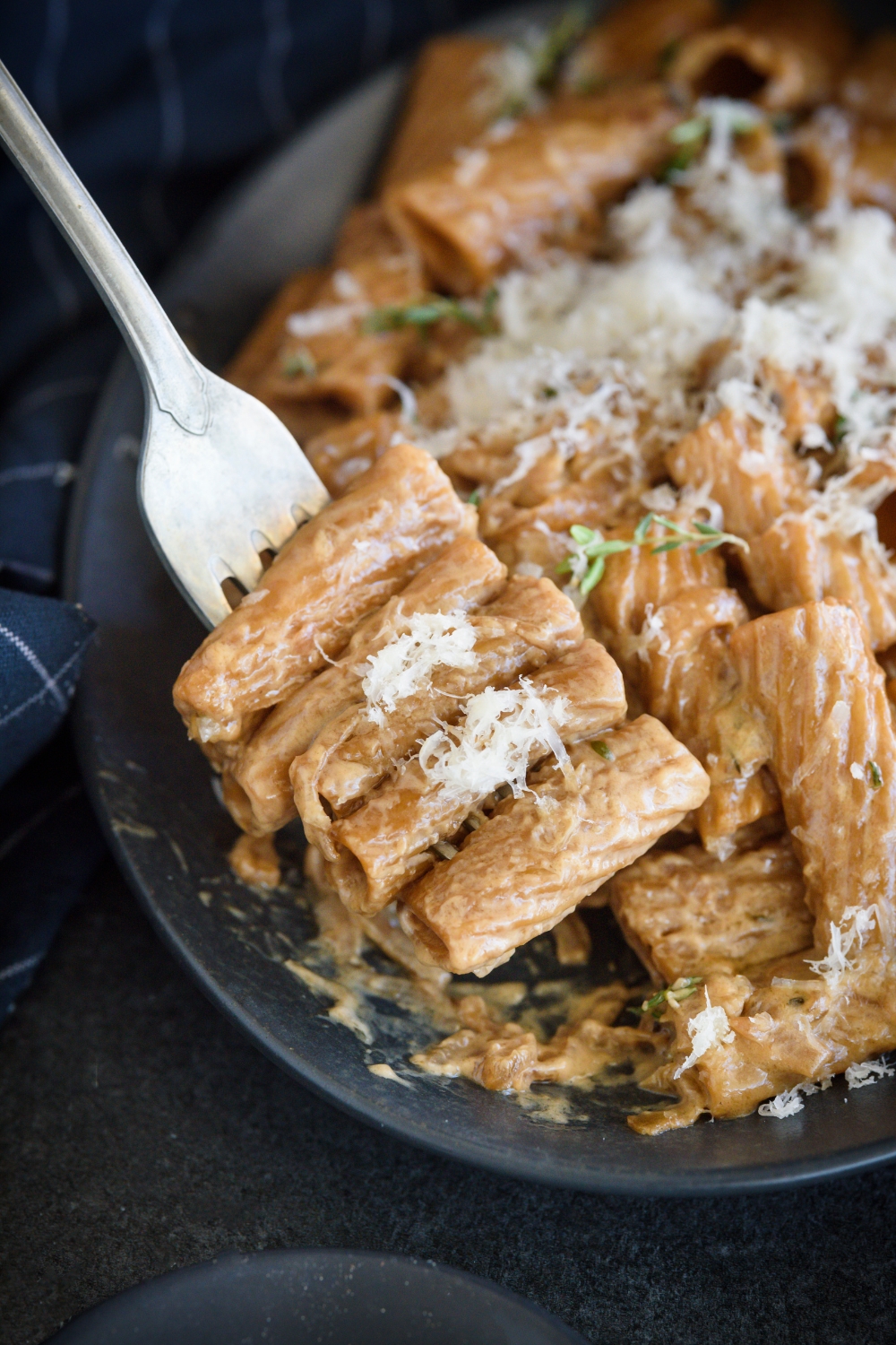 A fork holding four pieces of pasta covered in a brown cream sauce above a plate of pasta.