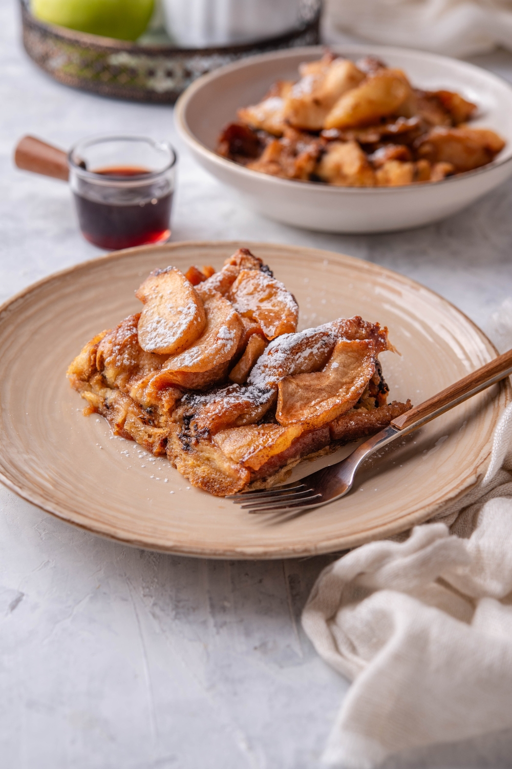 A serving of French toast covered in stewed apples and powdered sugar with a fork on the plate.