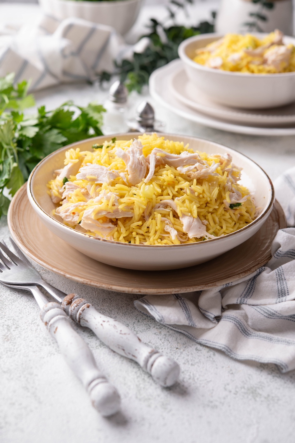 A bowl filled with yellow rice and cooked shredded chicken mixed together beside a set of silverware.