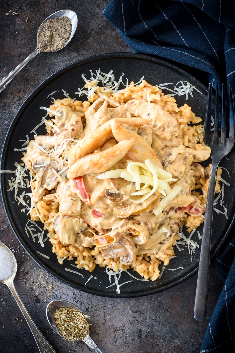 A plate of chicken in a cream sauce with red peppers, topped with shredded cheese on a bed of rice.