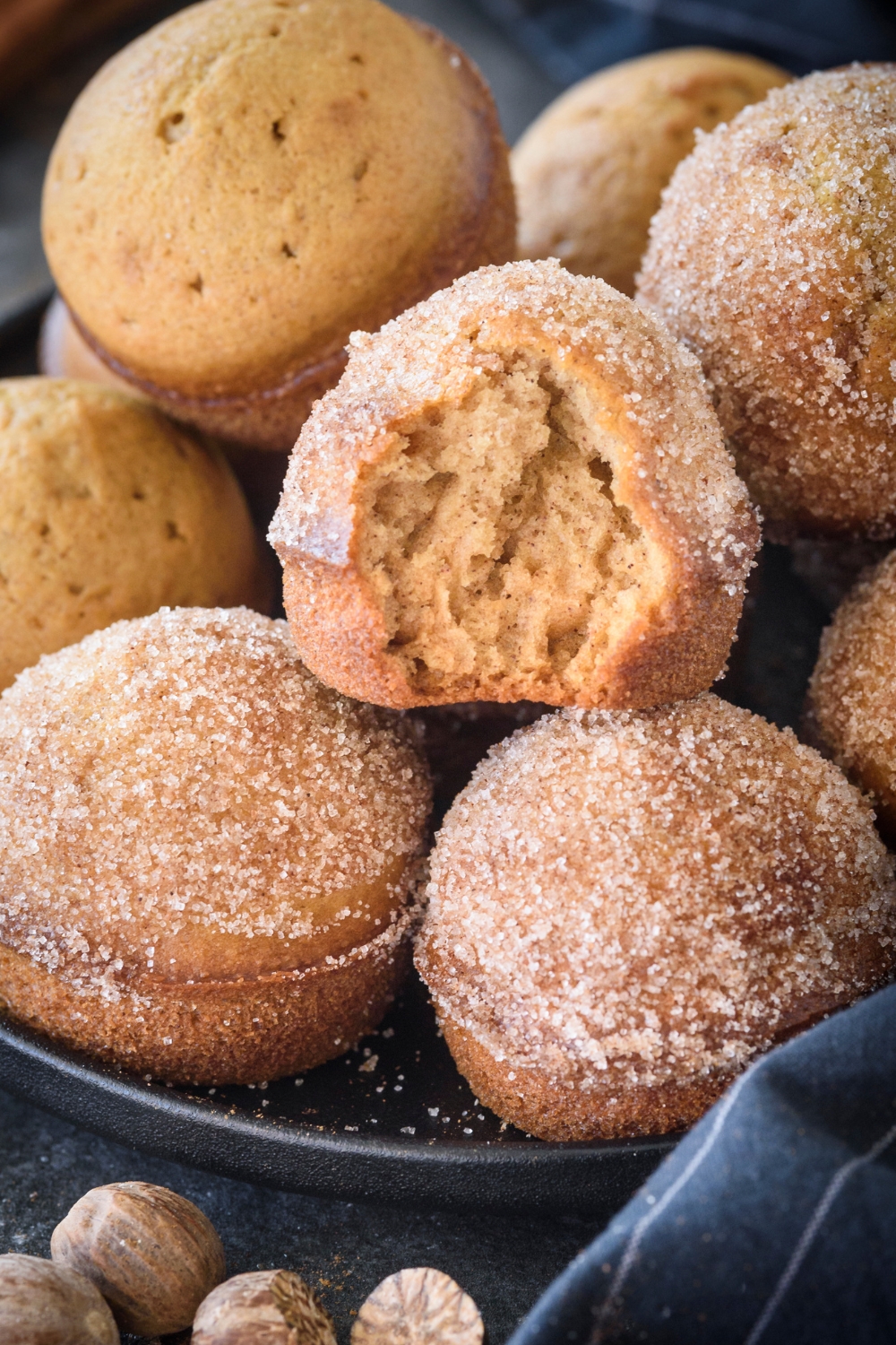 A pile of muffins with some covered in cinnamon sugar and one with a bite taken out of it.