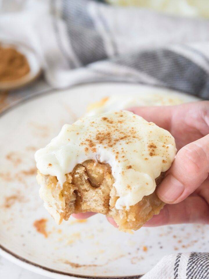 A cinnamon roll covered in cream cheese frosting and cinnamon with a bite taken out.
