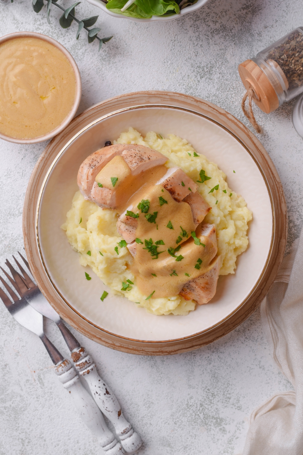 Overhead view of a plate of cooked and sliced chicken breast covered in a creamy brown sauce, garnished with fresh herbs, on a bed of mashed potatoes.