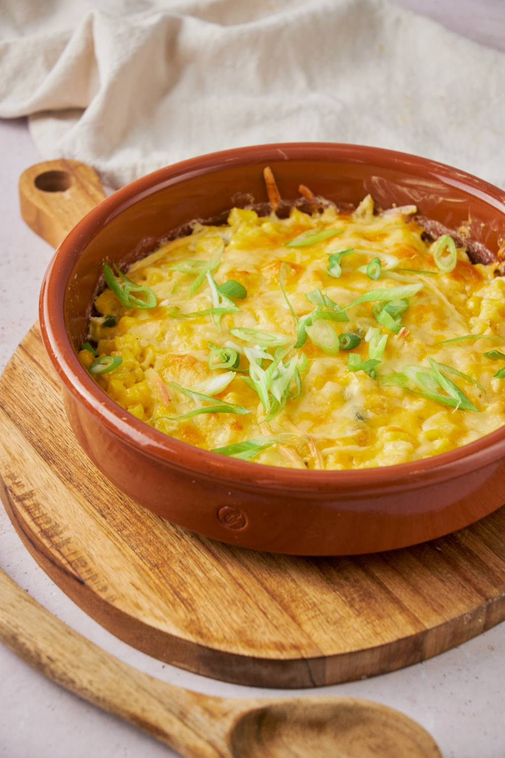 A red dish of cooked jalapeno corn casserole on a wooden serving platter