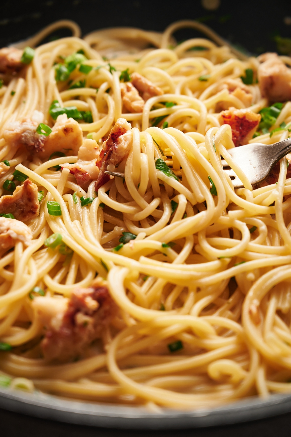 Cooked spaghetti mixed with lobster meat, green onion, and fresh herbs. There is a fork in the spaghetti.