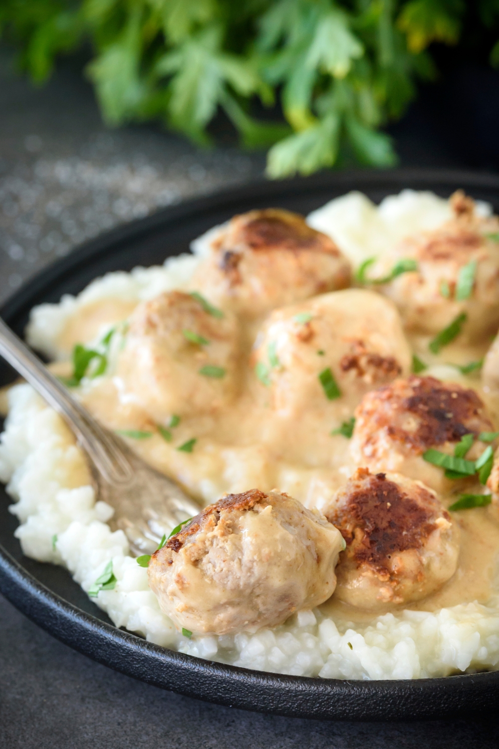A plate of meatballs covered in fresh herbs and creamy gravy on a bed of rice. There is a fork on the plate.