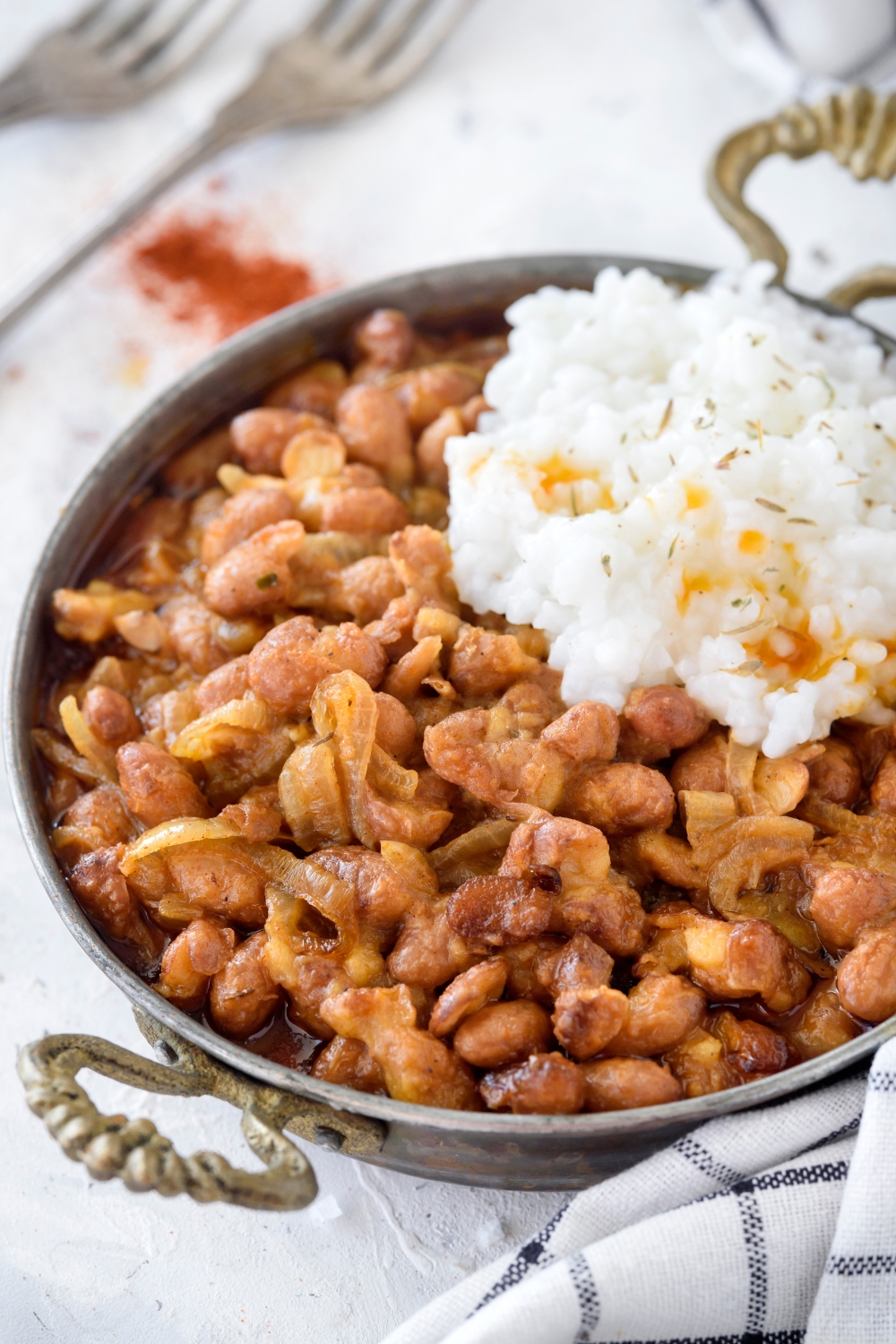 A bowl of cooked pinto beans mixed with cooked onions and a side of white rice.