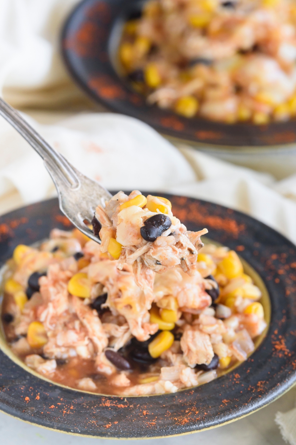 A fork holding a bite of southwest chicken casserole above a bowl filled with casserole.