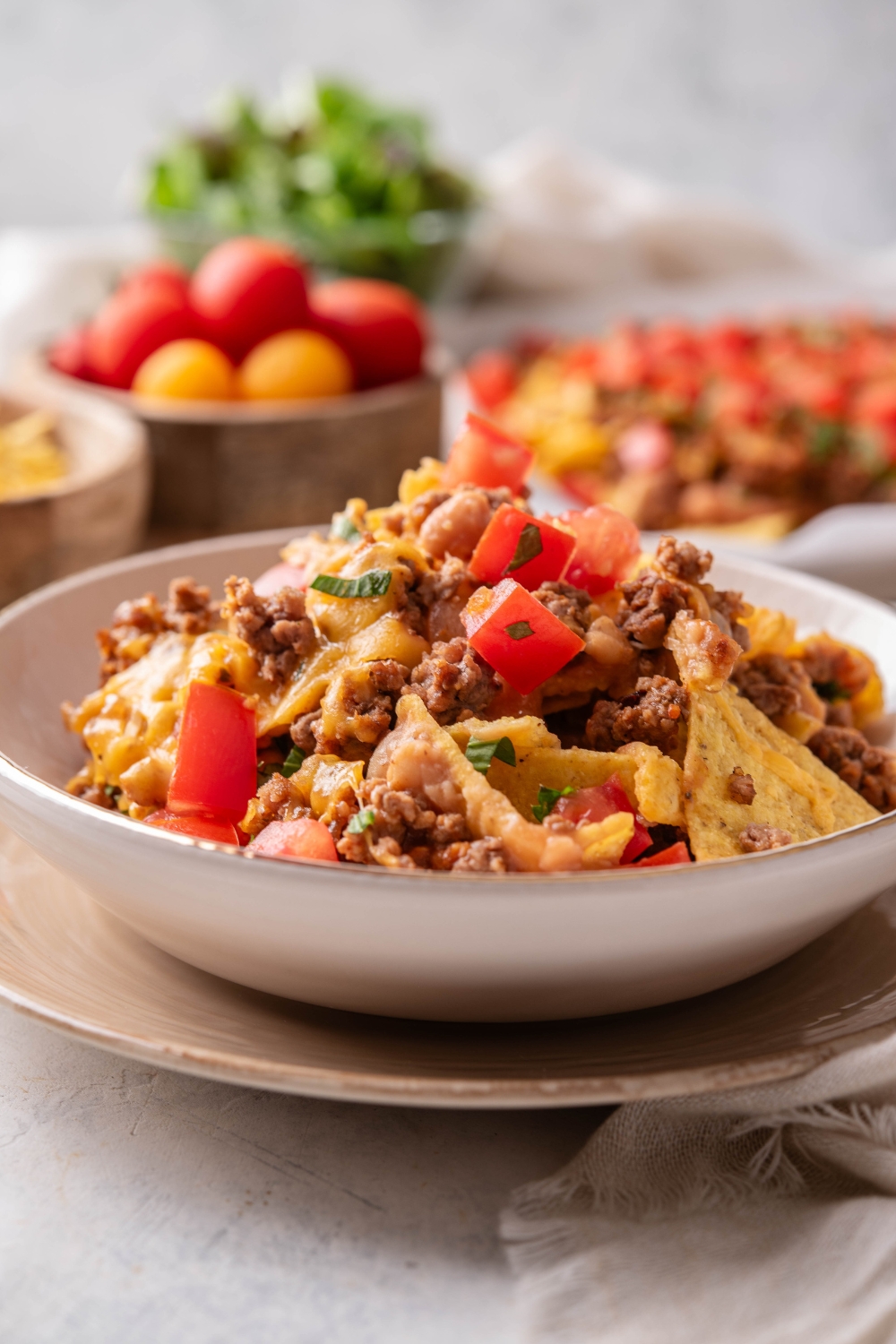 A bowl of beef nachos topped with diced tomatoes, beef, melted cheese, and cilantro.