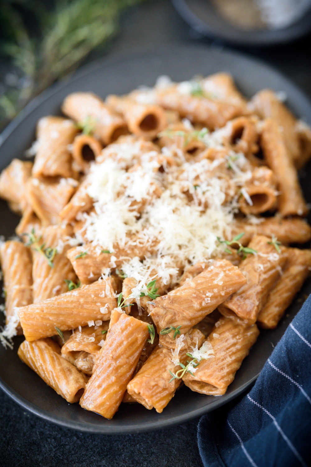 A plate of rigatoni pasta covered in a brown cream sauce and topped with fresh herbs and grated cheese.