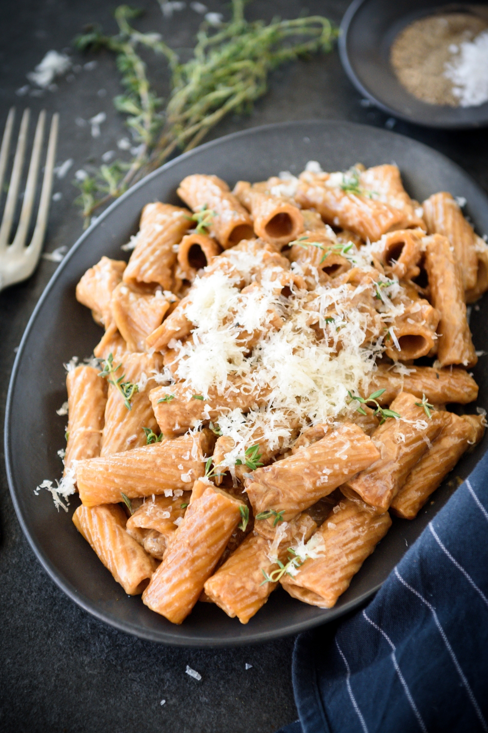 A plate of rigatoni pasta covered in a brown cream sauce and topped with fresh herbs and grated cheese.