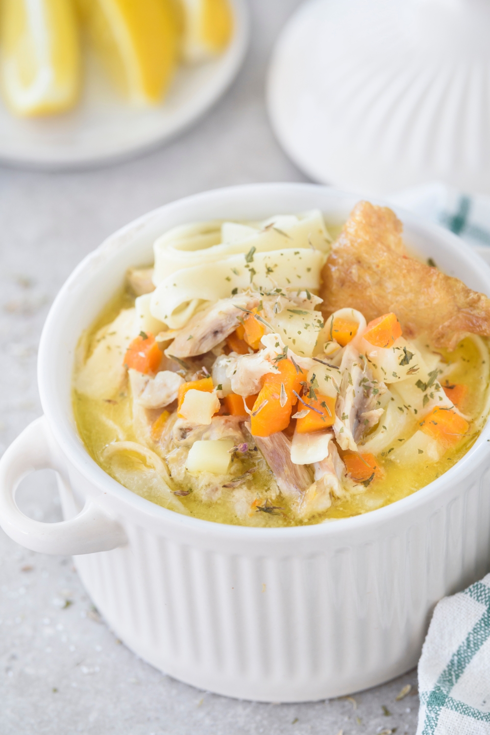 A bowl of chicken noodle soup with chunks of carrots, potatoes, and crispy chicken skin in the soup. The soup is garnished with herbs.