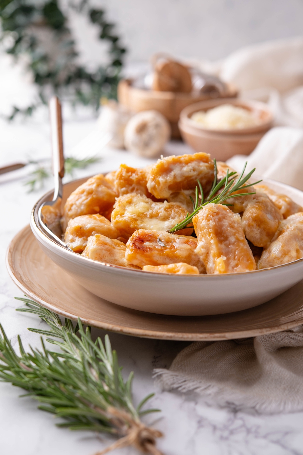 A bowl of sweet potato gnocchi covered in cream sauce with a sprig of rosemary garnished on top.