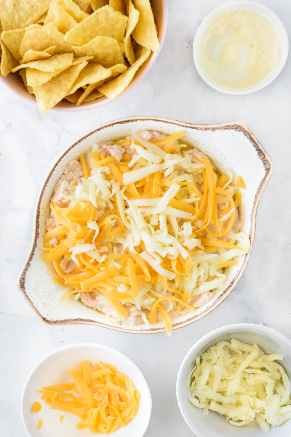A baking dish filled with dip and covered in shredded cheese.