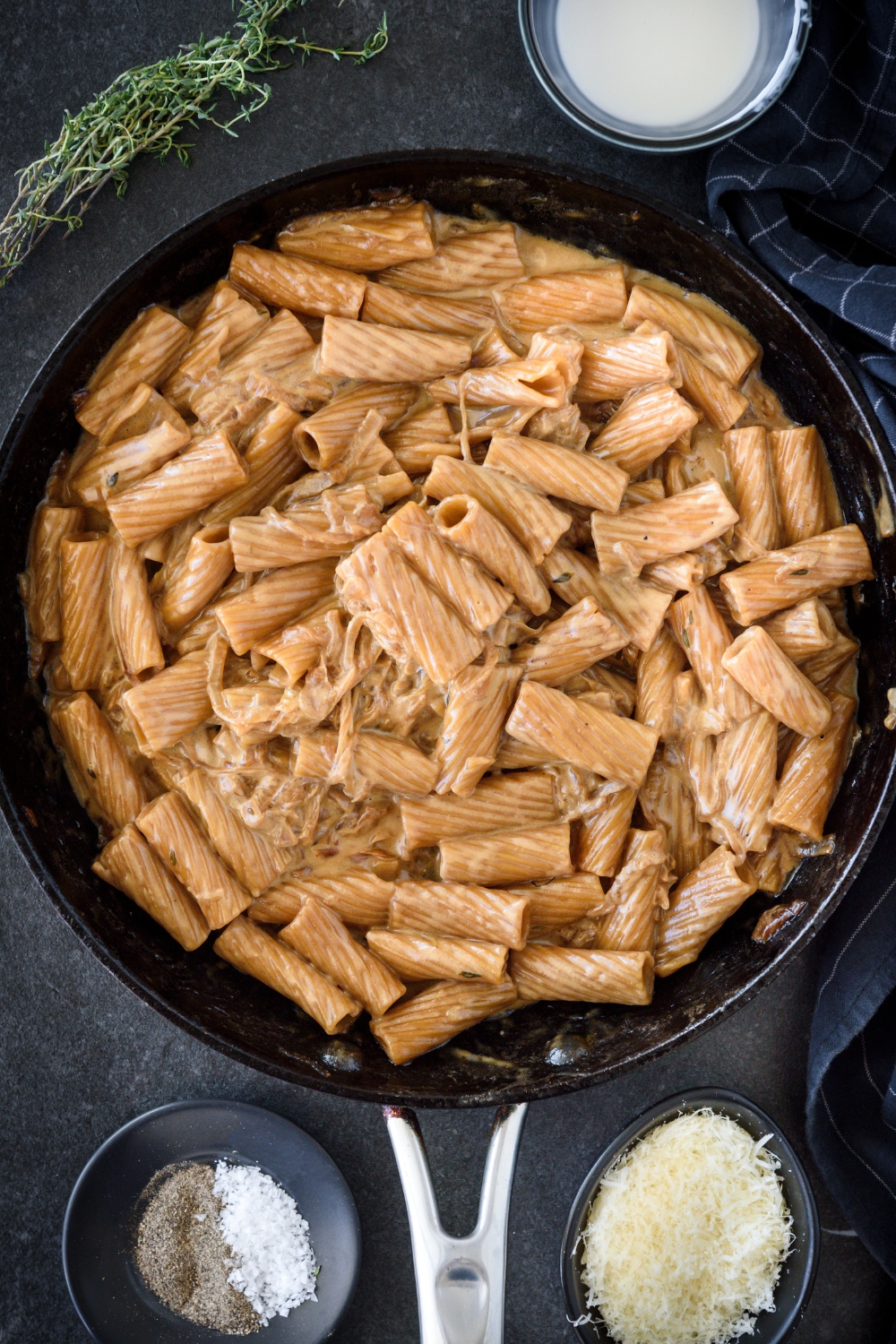 A skillet filled with cooked pasta tossed in a brown cream sauce with caramelized onions mixed in the pasta.