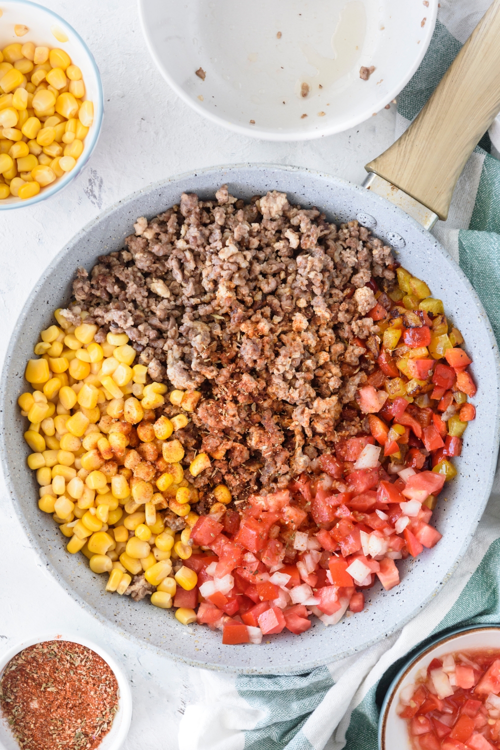 A skillet filled with cooked ground beef, seasoning, diced peppers, corn, and diced tomatoes and onions.