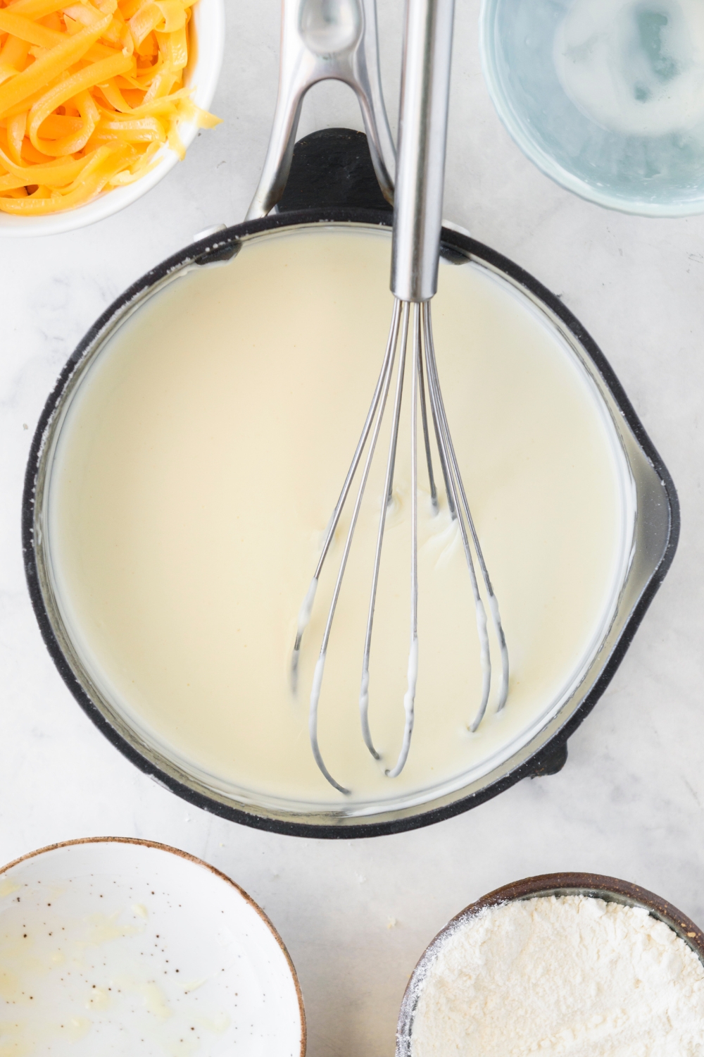 A pan filled with cream sauce and a whisk is in the pan.