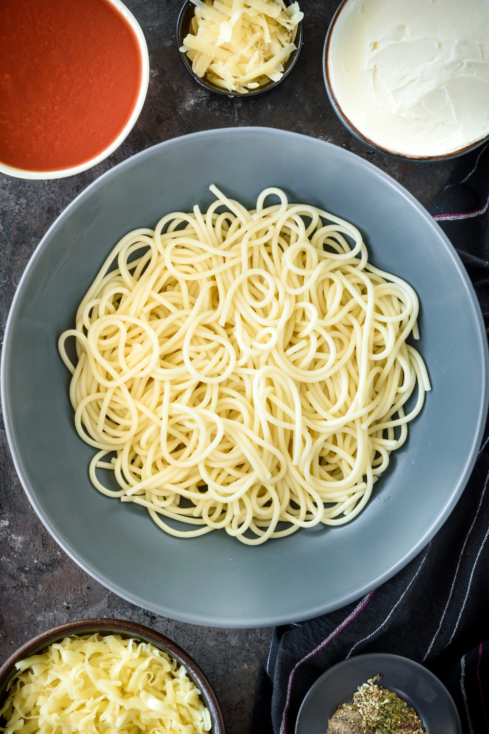 A bowl of cooked spaghetti noodles surrounded by an assortment of ingredients.