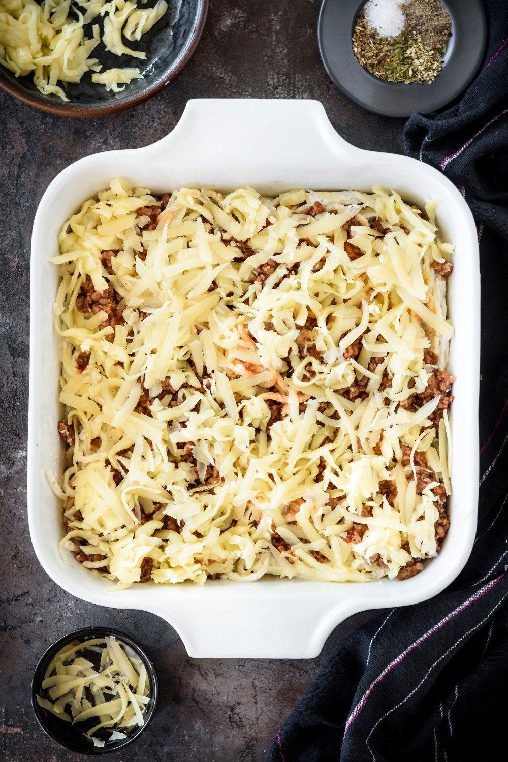 A baking dish filled with spaghetti and cooked ground beef, covered in shredded cheese.