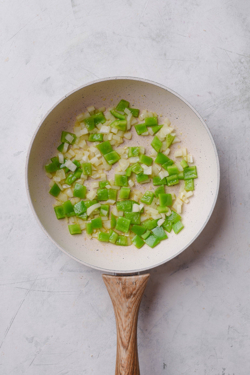 A skillet with diced onion and green bell peppers cooking in it.