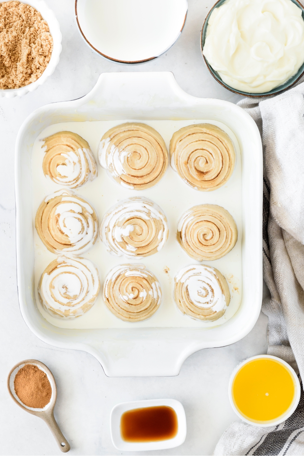 A baking dish filled with nine evenly-spaced cinnamon rolls and cream poured on top.