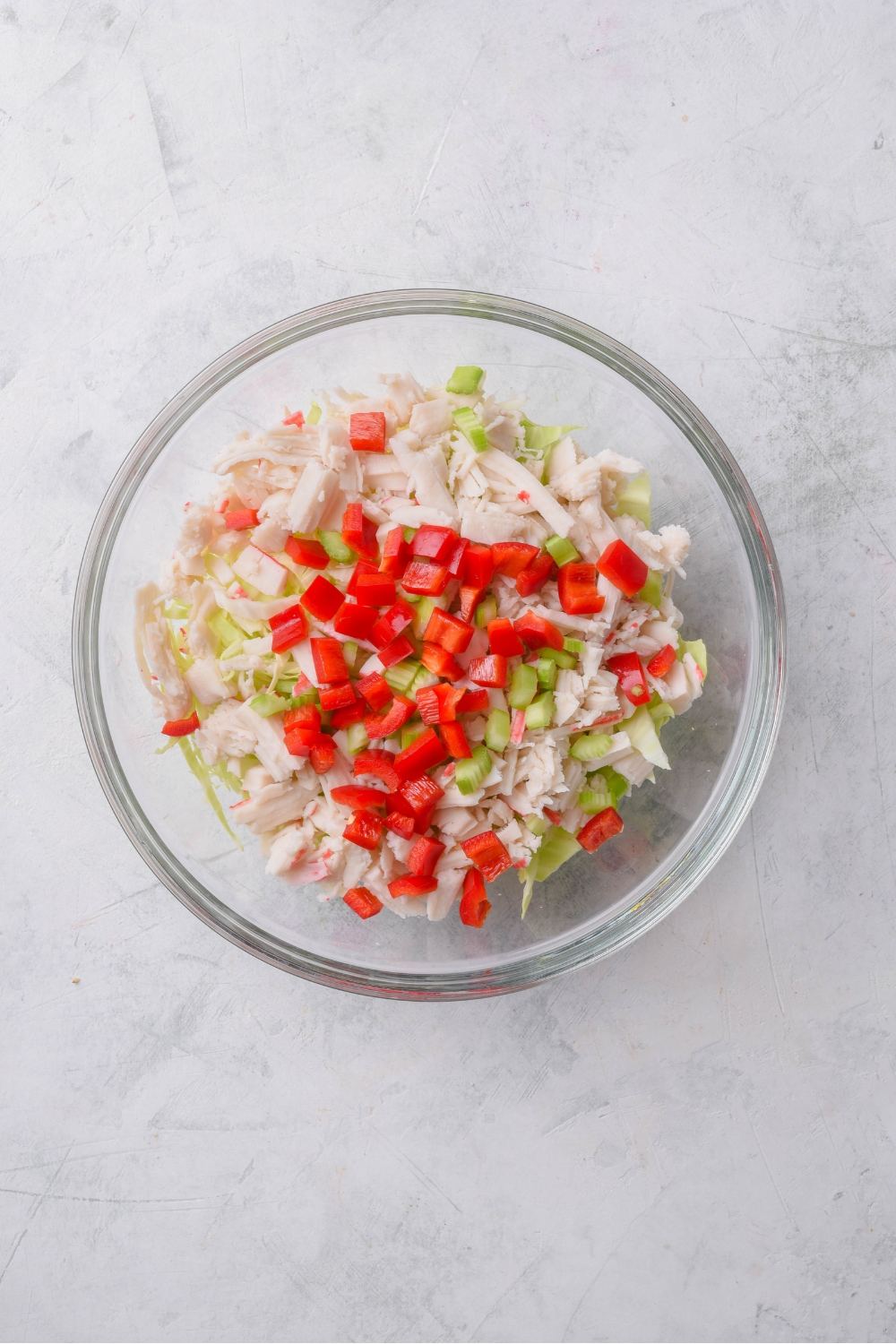 A clear bowl filled with crab meat, diced red peppers, and diced celery.