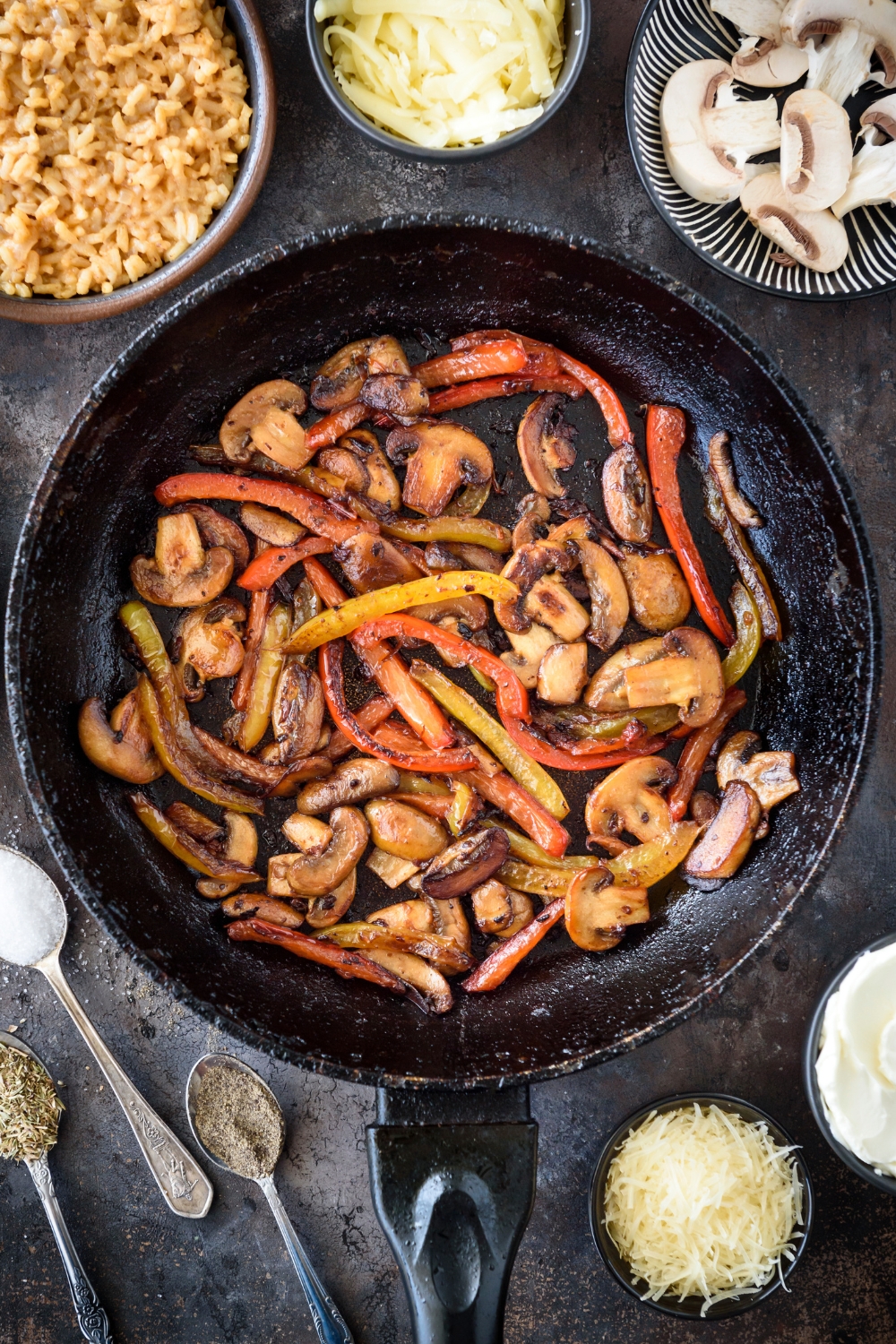 A skillet filled with cooked and sliced red peppers, yellow peppers, and mushrooms.