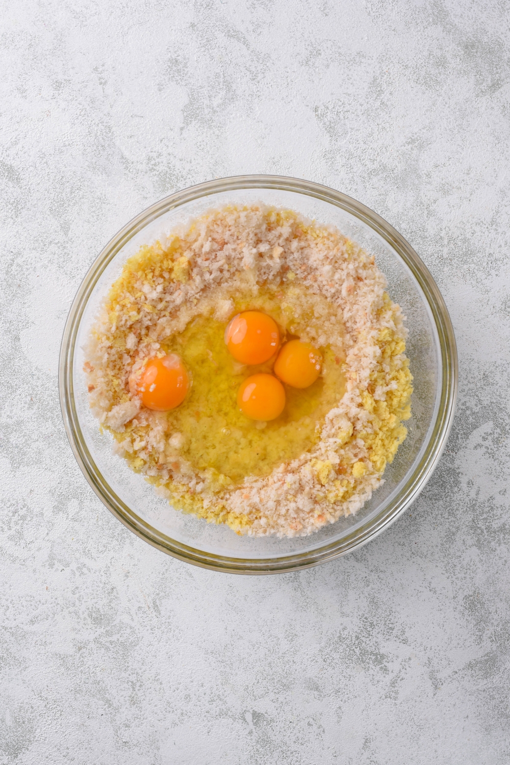 A clear bowl filled with cornbread crumbles, bread crumbs, and four whole eggs.
