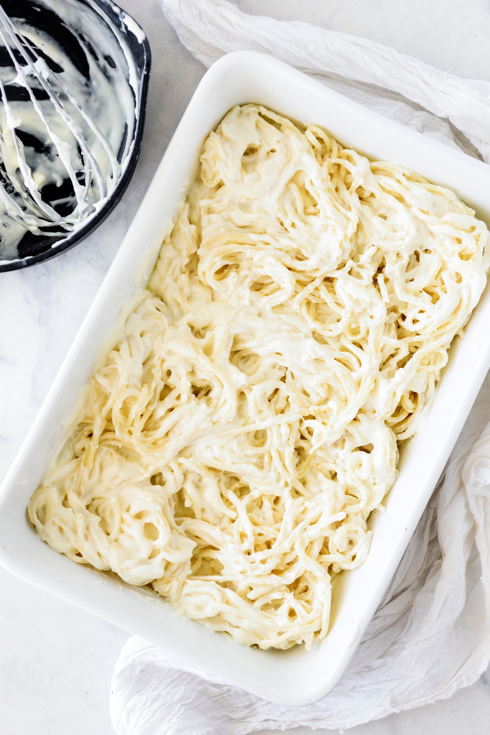 A baking dish filled with cooked spaghetti and Alfredo sauce.