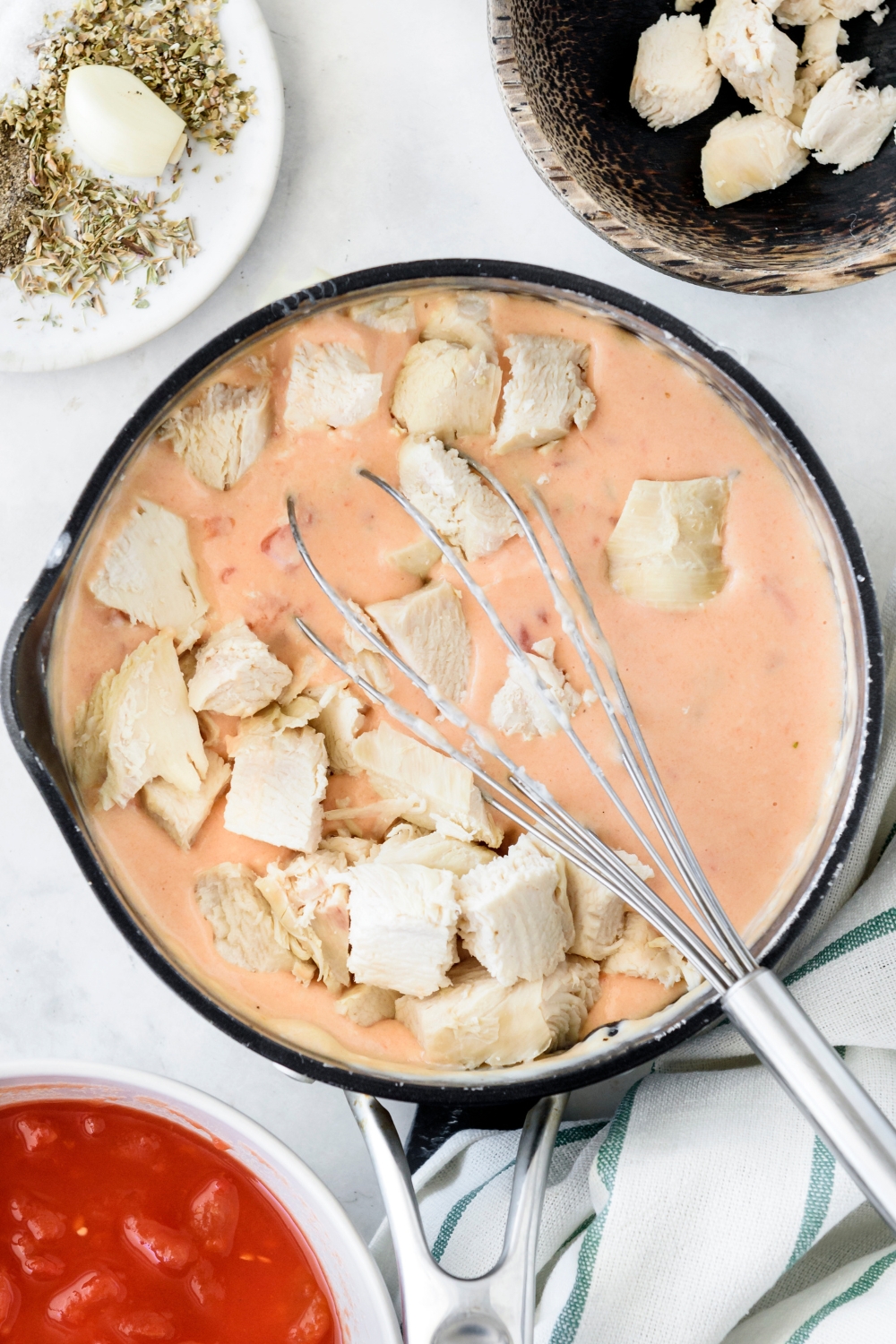 A pan filled with a pink cream sauce and diced chicken being tossed in the cream sauce using a whisk.