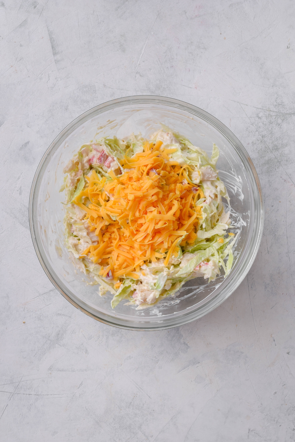 A clear bowl filled with creamy crab meat, sliced cabbage, and a pile of shredded cheese on top.