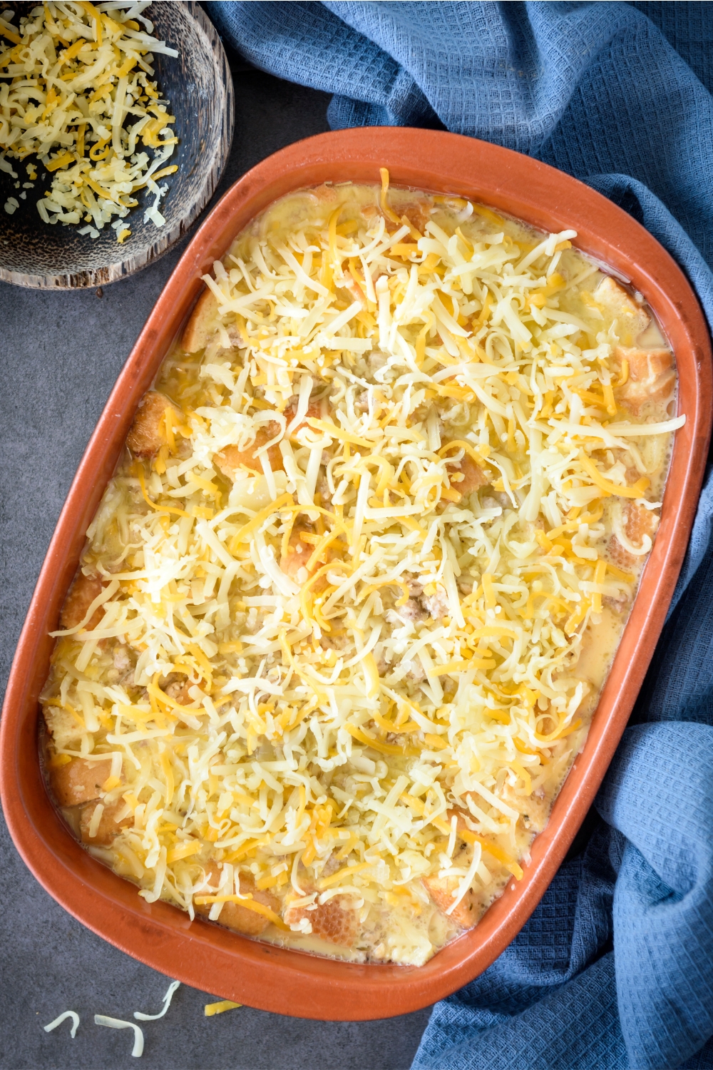 A baking dish filled with unbaked casserole topped with shredded cheese.