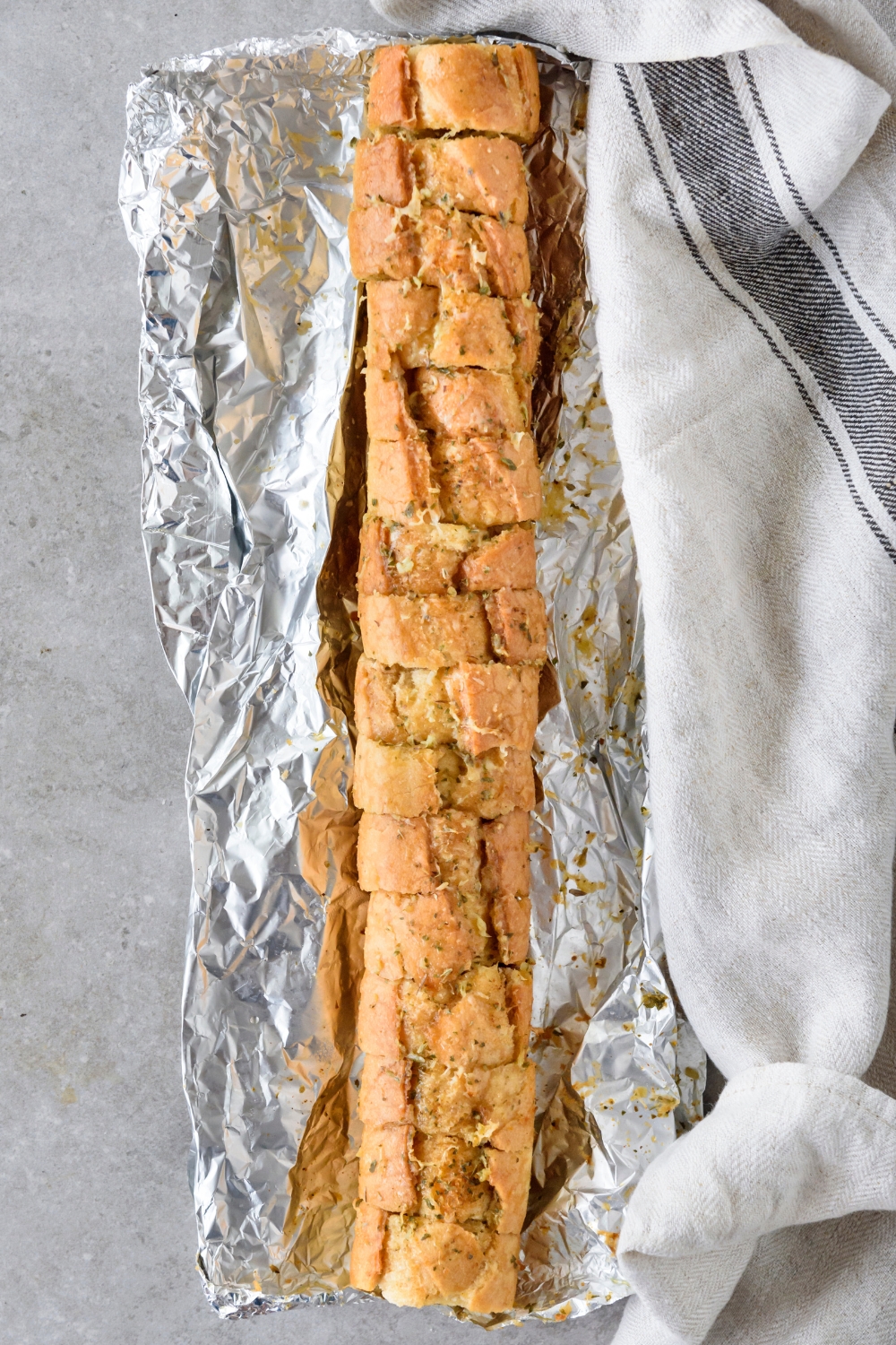 A baguette that has been sliced into thin slices and toasted. The baguette is on a sheet of aluminum foil.