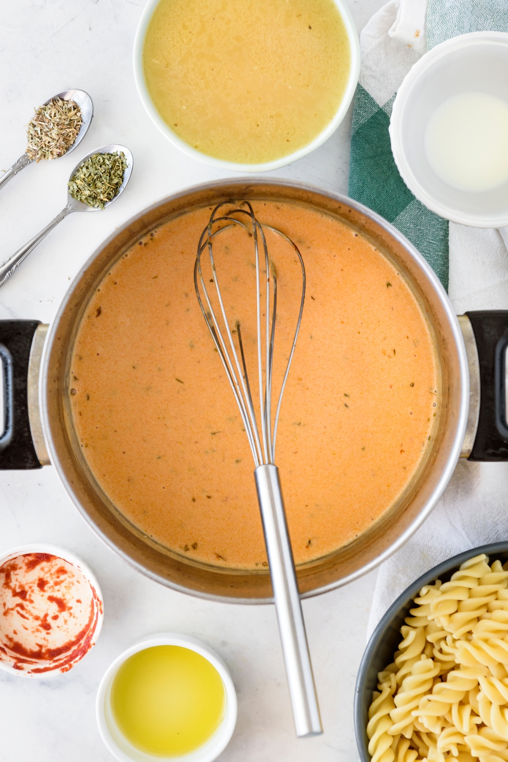 A pot filled with a red cream sauce and a whisk is balanced above the pot.