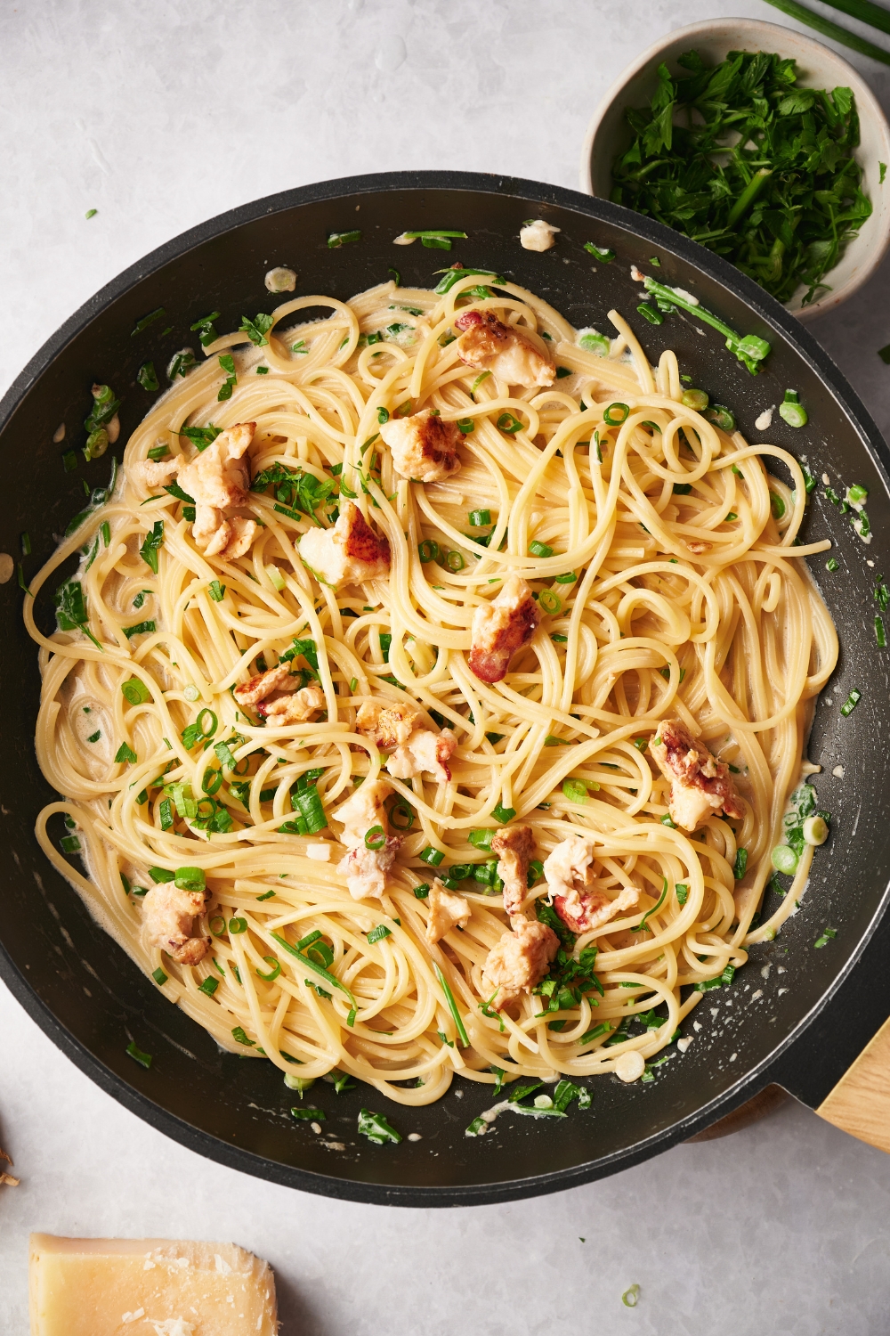 A skillet with cooked spaghetti and lobster meat in a cream sauce garnished with fresh herbs and green onion.