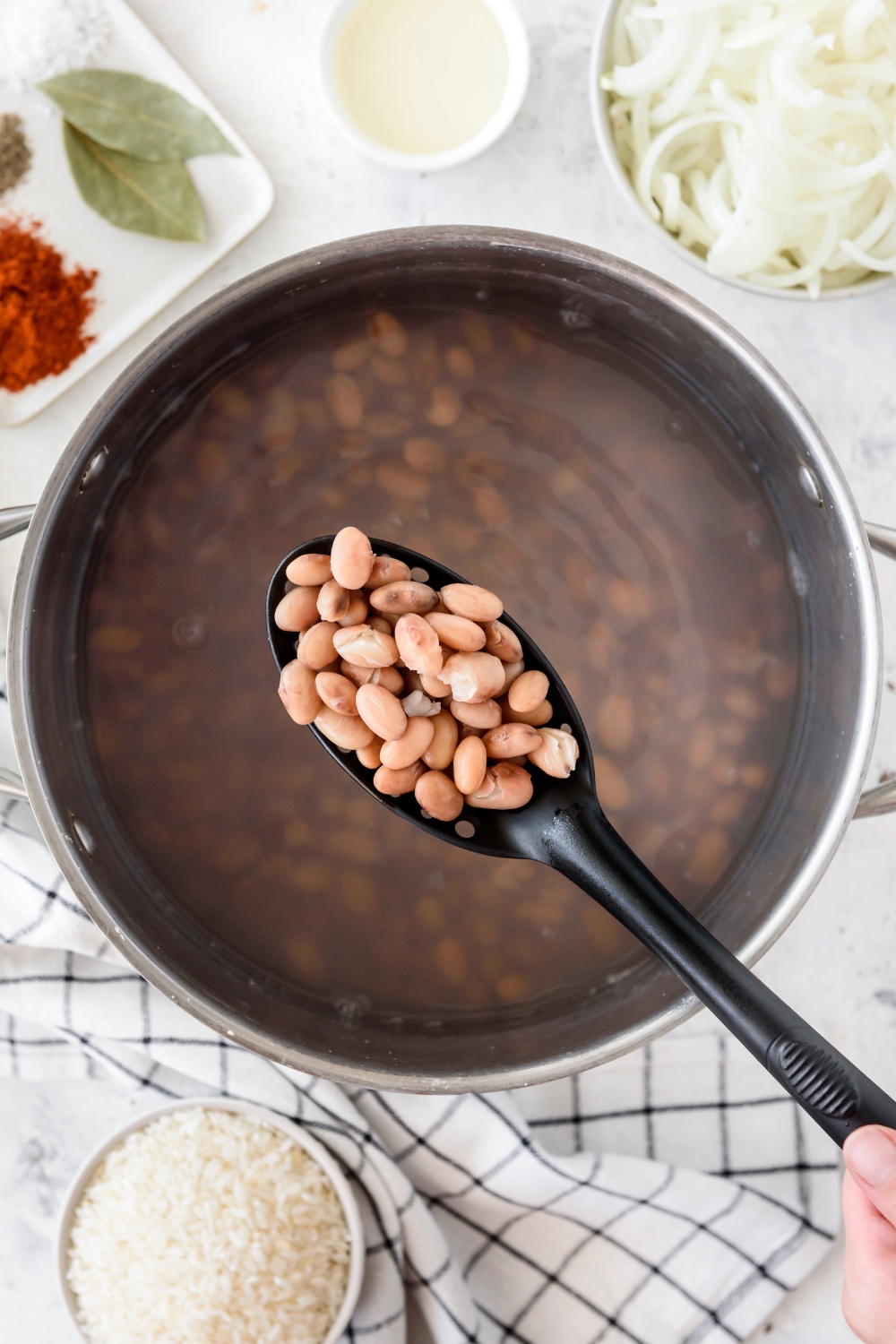 A straining spoon with a spoonful of beans held above a pot filled with beans in water.