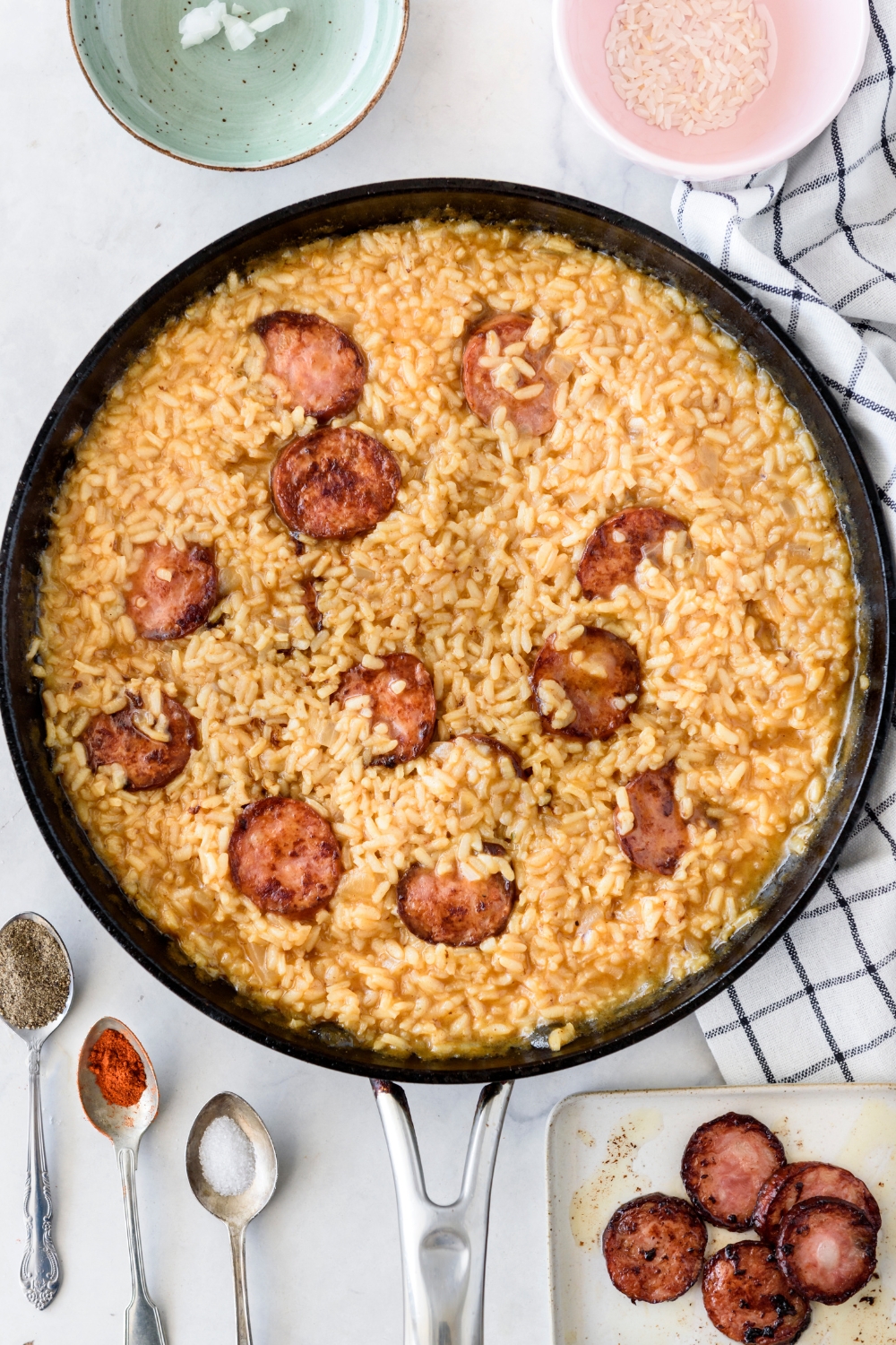 A skillet filled with dirty rice and cooked sausage slices placed on top of the rice.