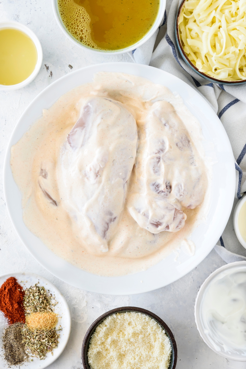 A shallow plate filled with two raw chicken breasts covered in a sour cream marinade.