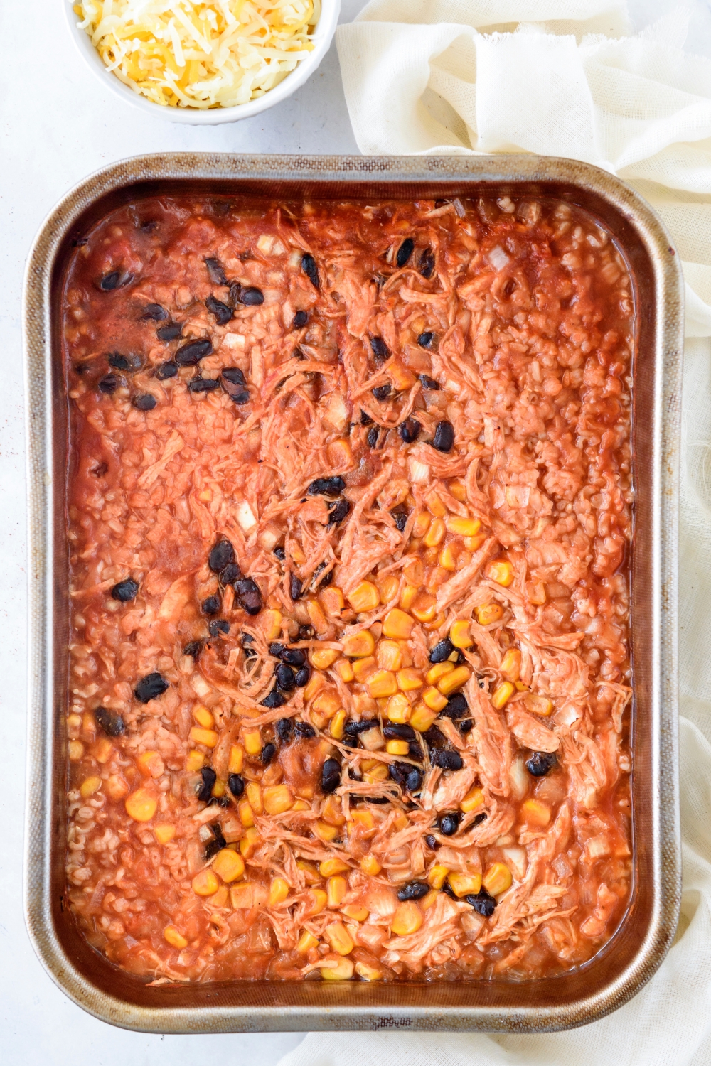 baking dish filled with shredded chicken, black beans, corn, and diced onion in a tomato sauce.