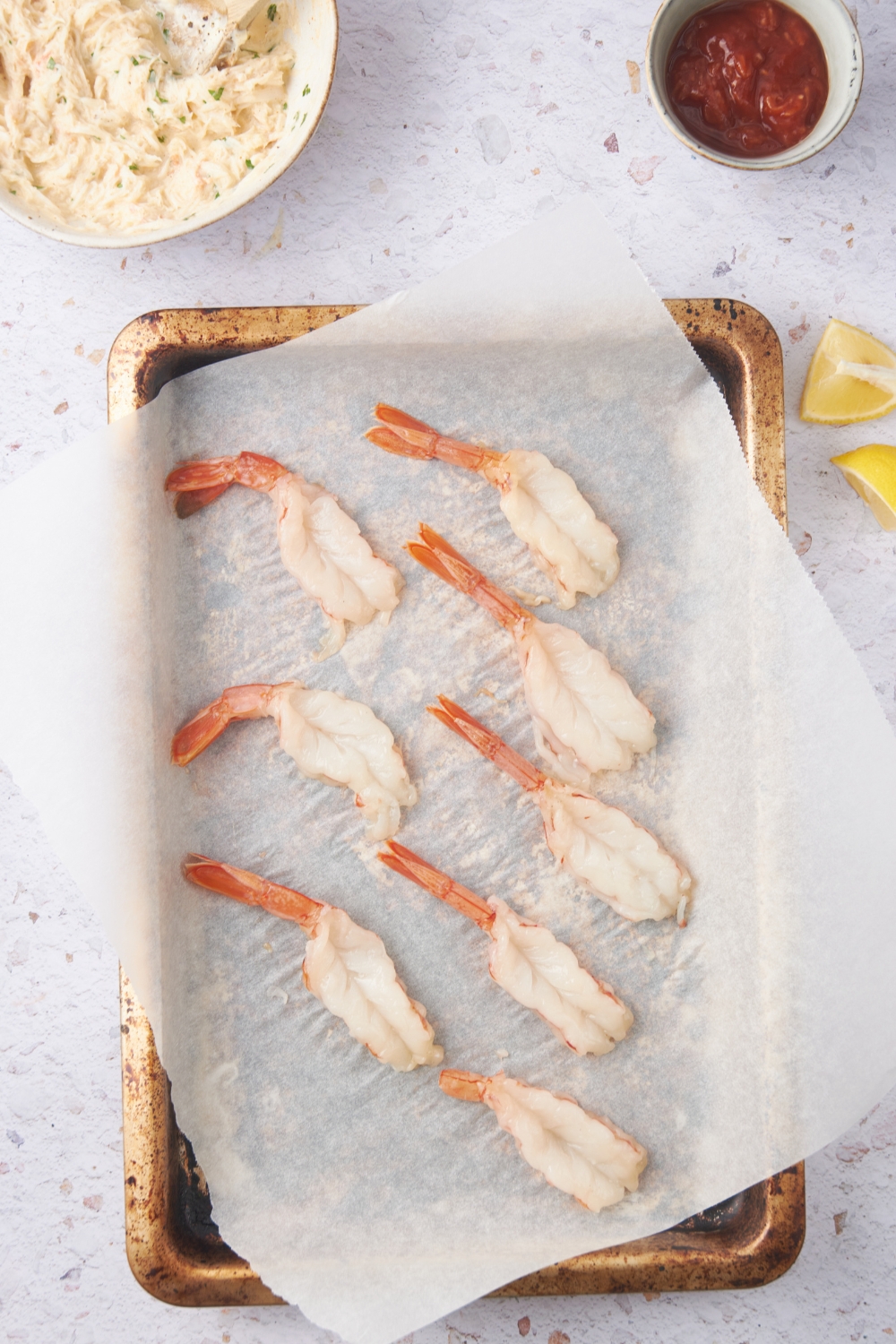 A baking sheet lined with parchment paper with eight butterflied shrimp on it.