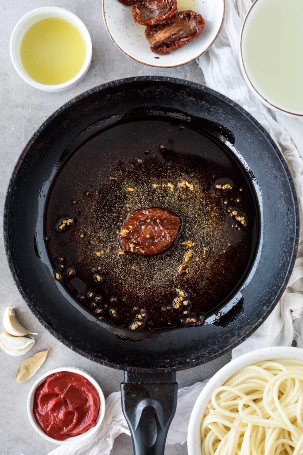 A skillet with oil, minced garlic, and a sundried tomato in the skillet.