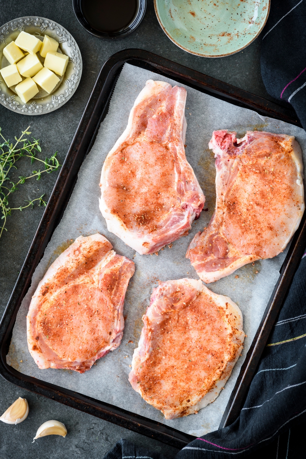 Four raw pork chops seasoned and placed on a baking sheet lined with parchment paper.