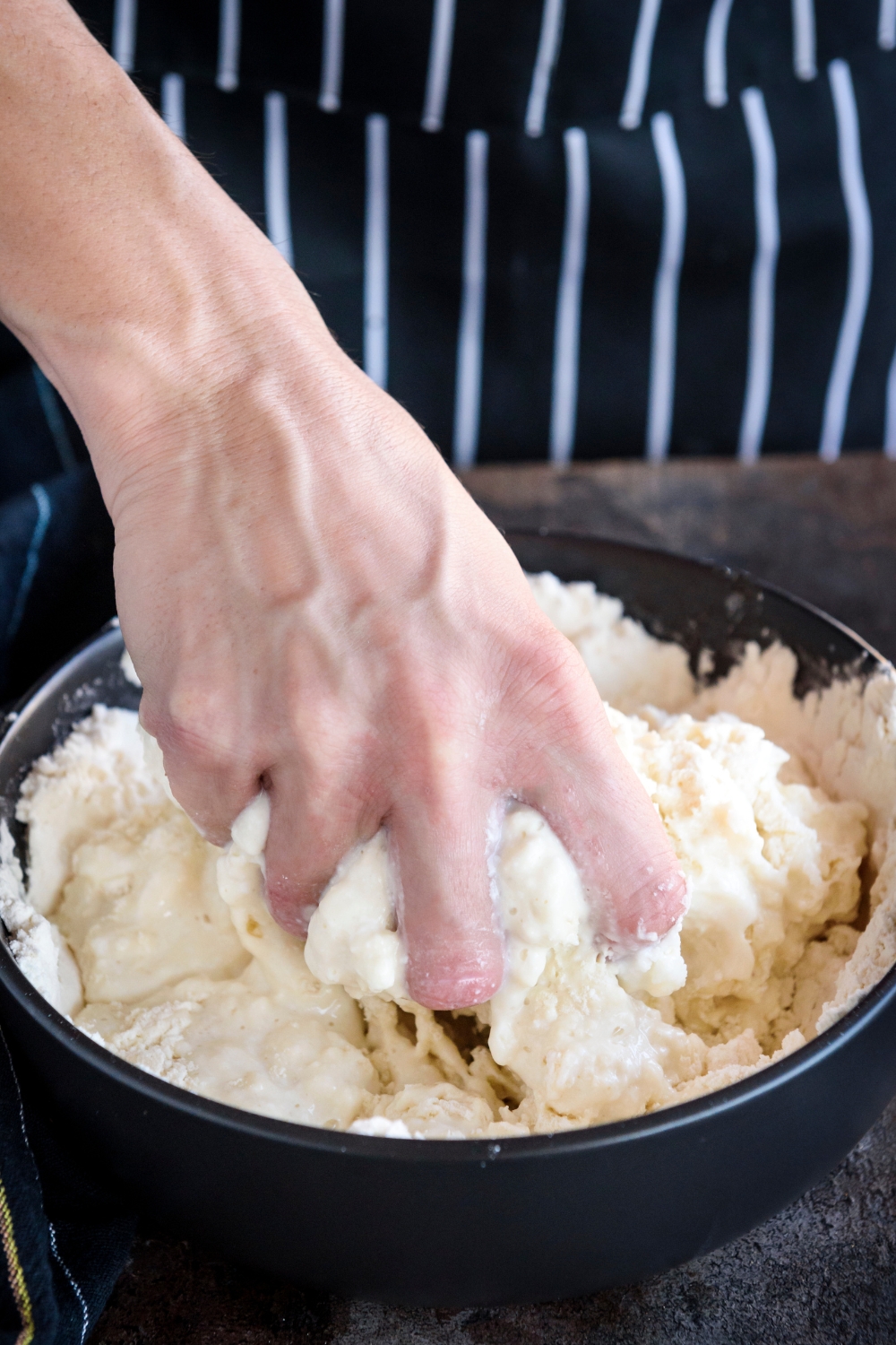 A hand mixing dough in a black bowl.