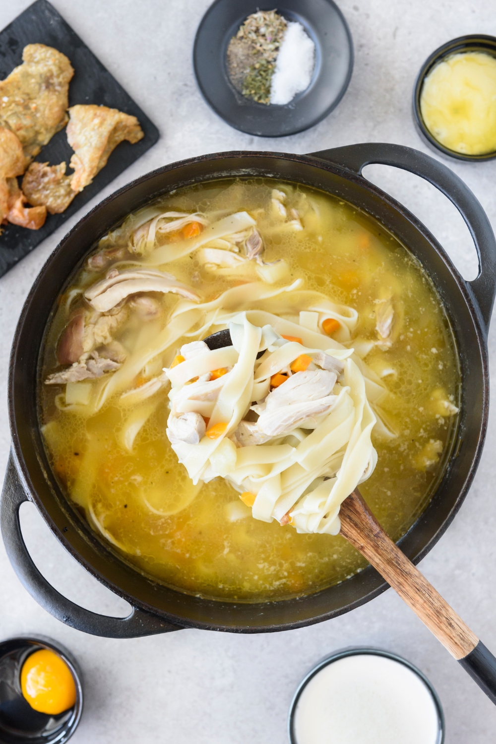 A large spoonful of chicken and noodles held above a pot filled with chicken noodle soup.