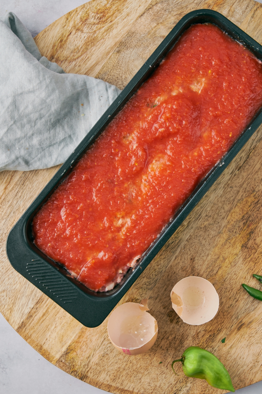 A loaf pan filled with unbaked meatloaf covered in red sauce.